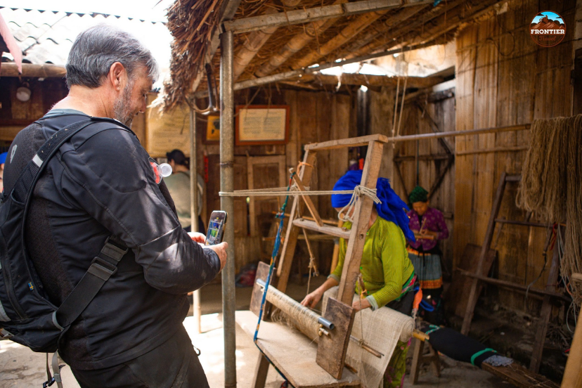 Visitors watching Hmong artisans weave colorful hemp textiles in Lung Tam, a renowned craft village in Ha Giang.