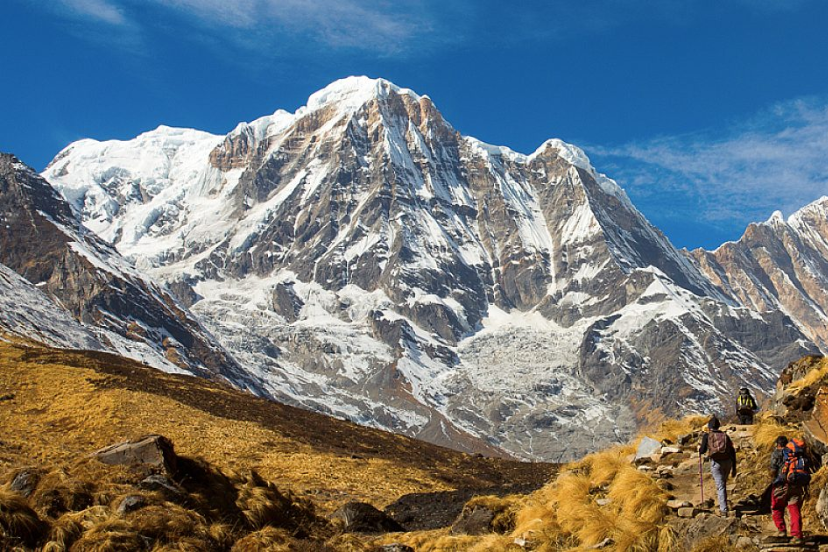  “Hikers approaching snowy peaks of Annapurna Sanctuary under clear Himalayan skies”