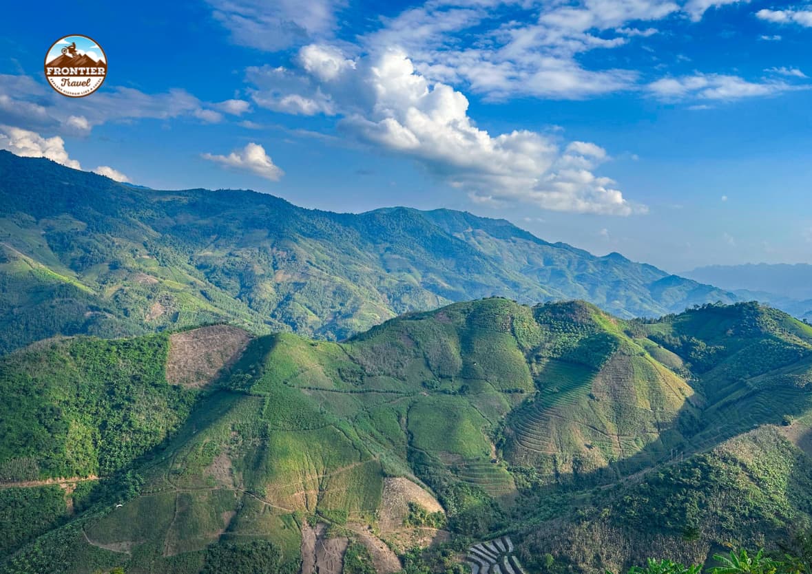 A cinematic wide shot of a lone rider carving through the limestone pinnacles of the Ha Giang Loop at sunset.